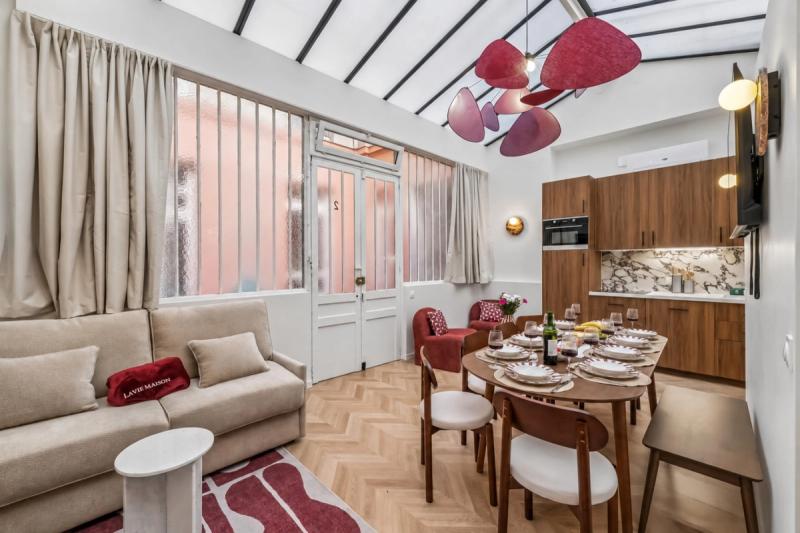 Open-plan living and dining space under a glass roof with herringbone parquet and sculptural pink pendant lights.