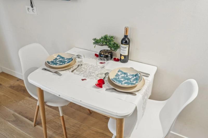 Dining nook with a white table set for two, bonsai centerpiece, and a bottle of Bordeaux.