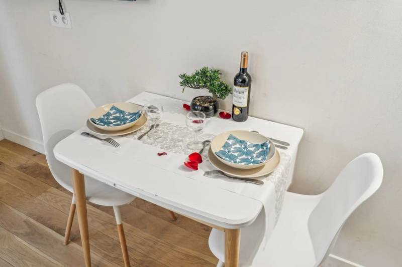 Dining nook with a white table set for two, bonsai centerpiece, and a bottle of Bordeaux.