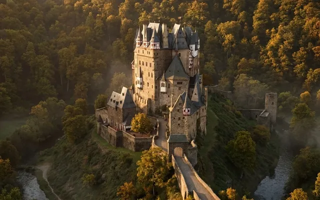Burg Eltz erhebt sich auf einem Felsen im Wald, umgeben vom Elzbach, mit ihren charakteristischen Türmen im goldenen Licht