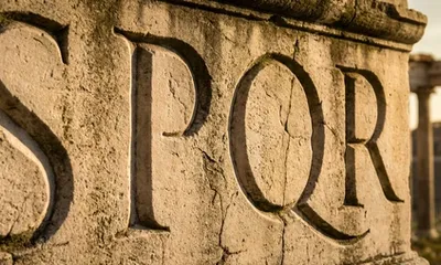 The letters SPQR are carved into a weathered ancient Roman stone archway, the Roman Forum visible behind it