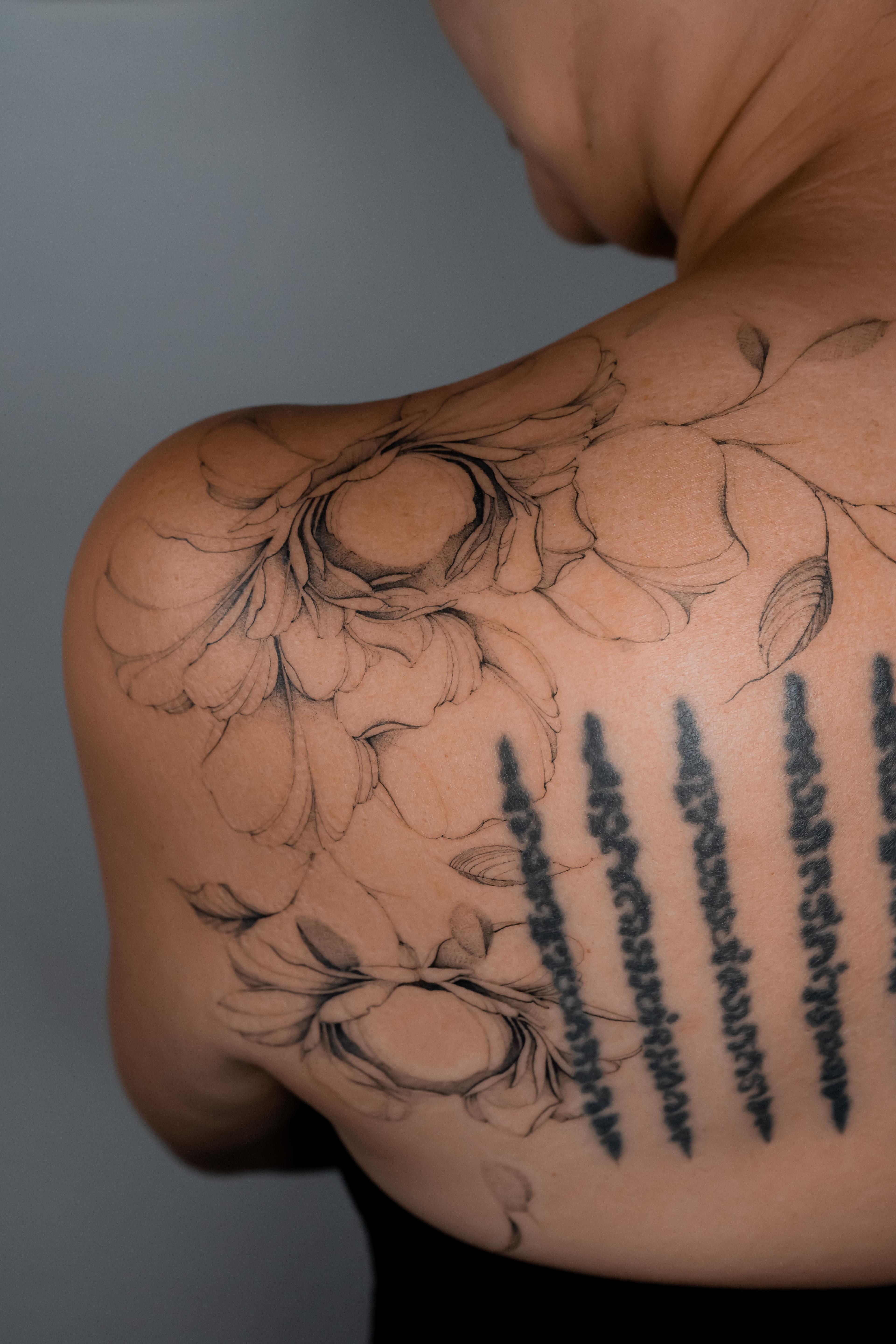 Fine-line peonies wrapping across the shoulder and upper back