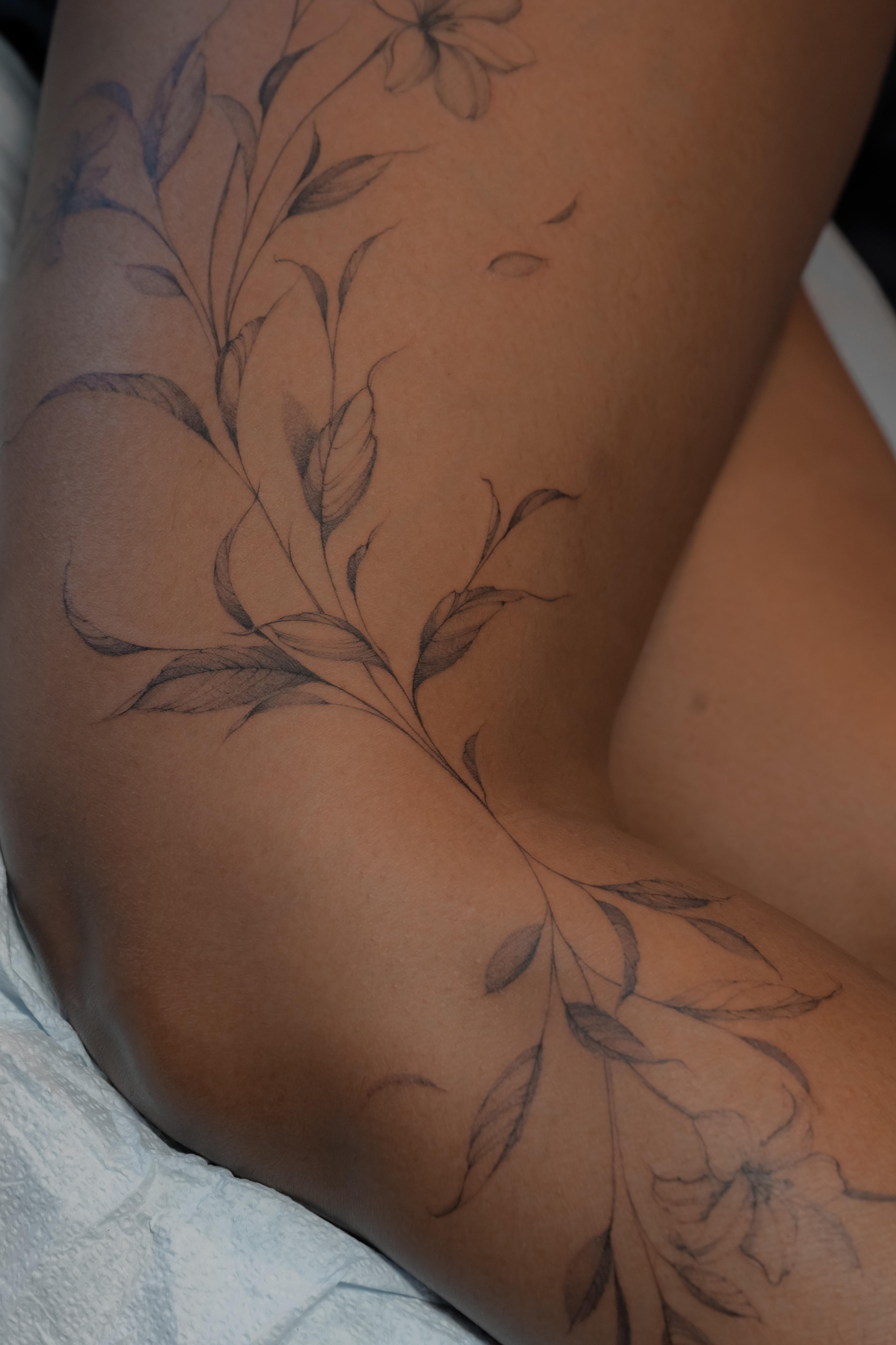 Fine-line lilies and long leaves flowing across the thigh and knee
