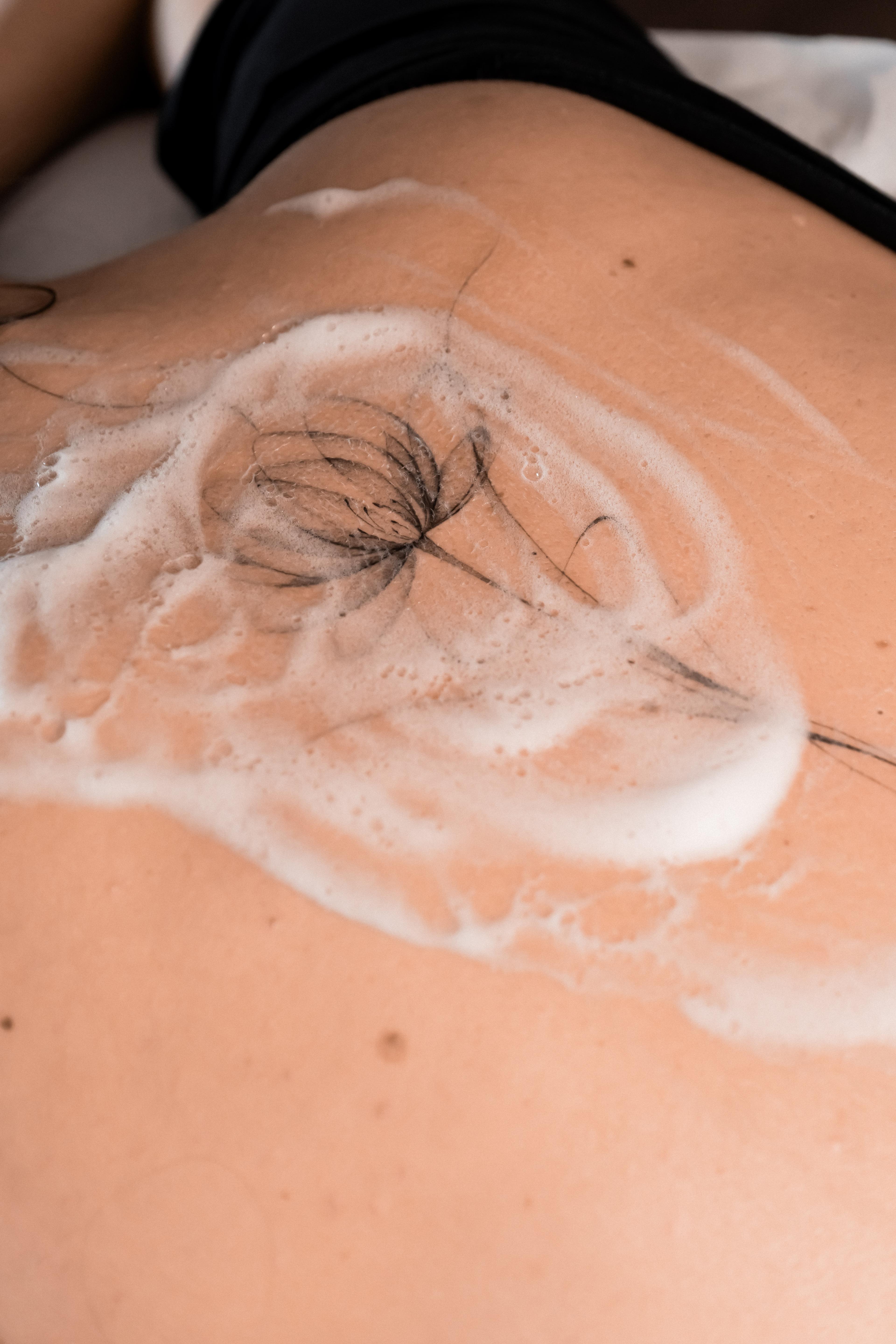 Fresh fine-line flower tattoo across the upper back during the final wash