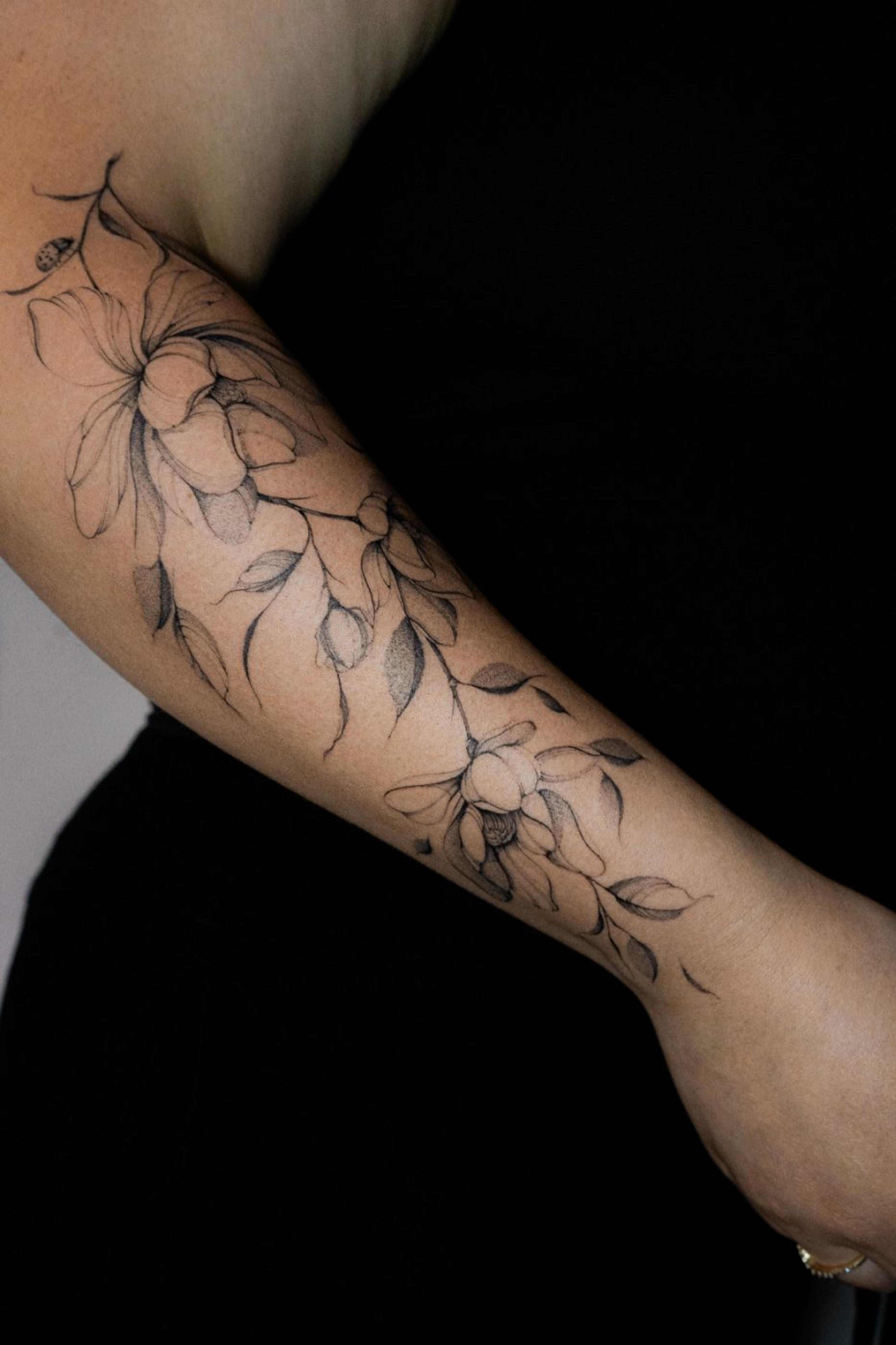 Fine-line magnolia and falling leaves with a small ladybug on the forearm