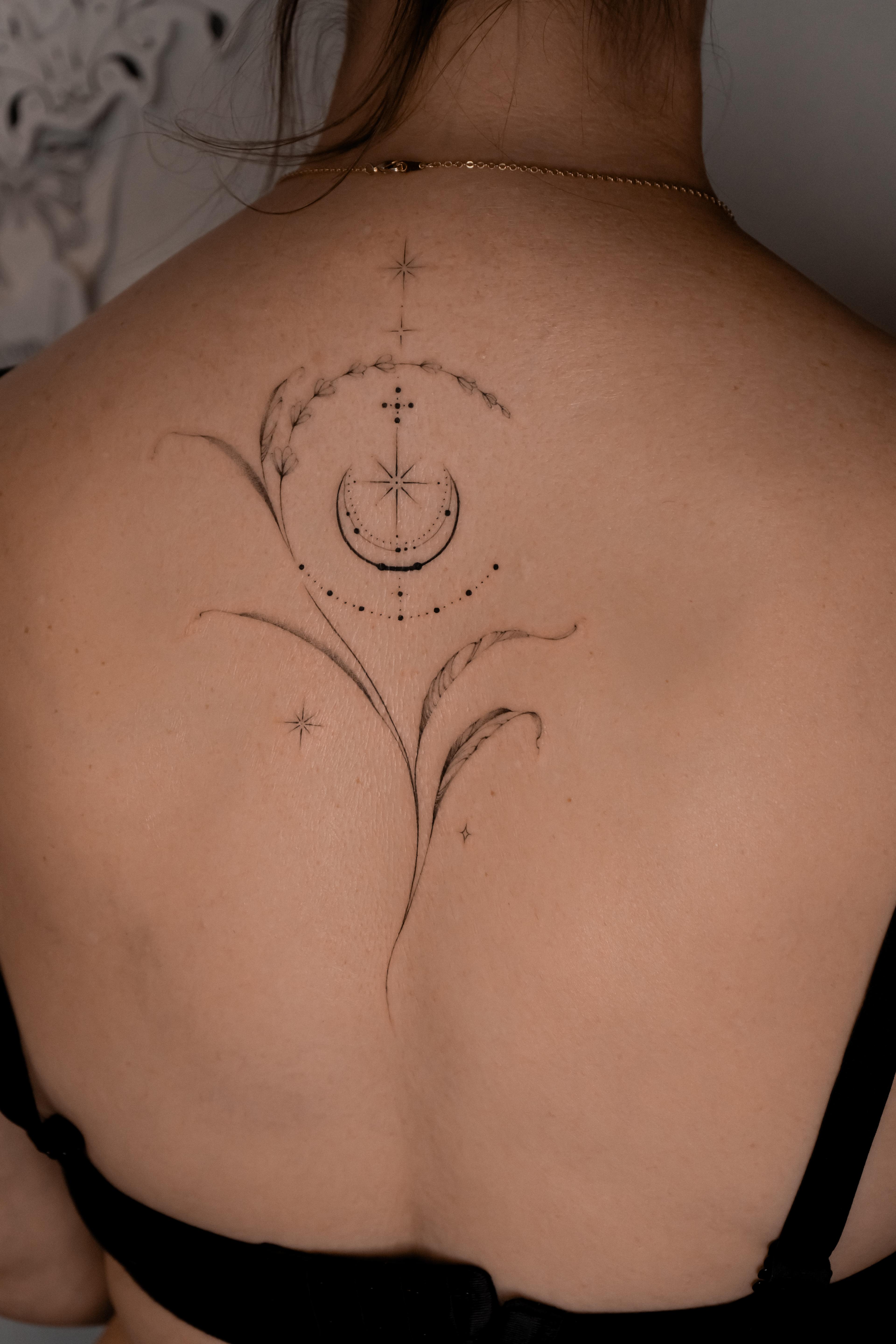 Fine-line crescent moon, stars and a long botanical stem on the upper back