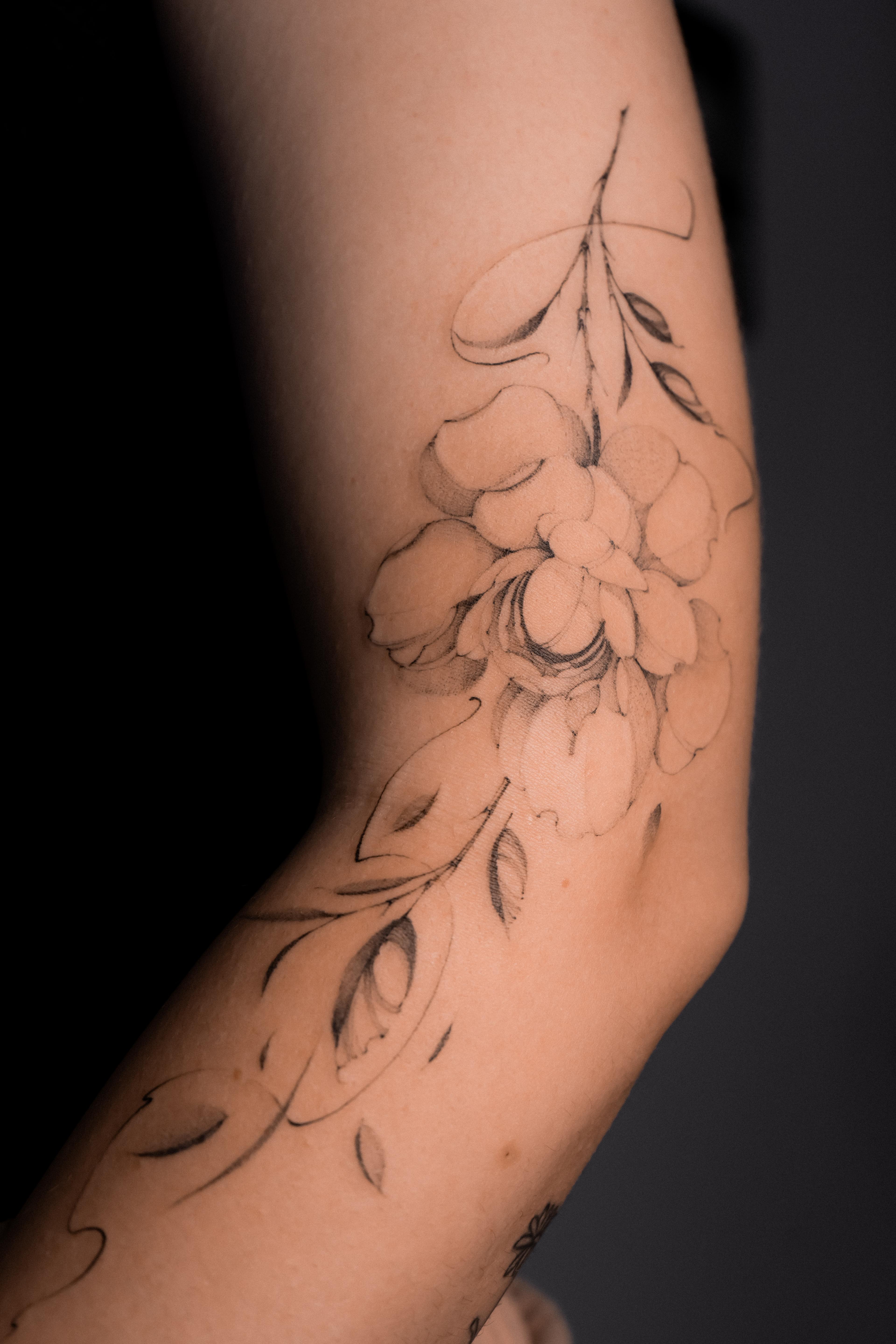 Fine-line peony branch wrapping around the forearm and elbow