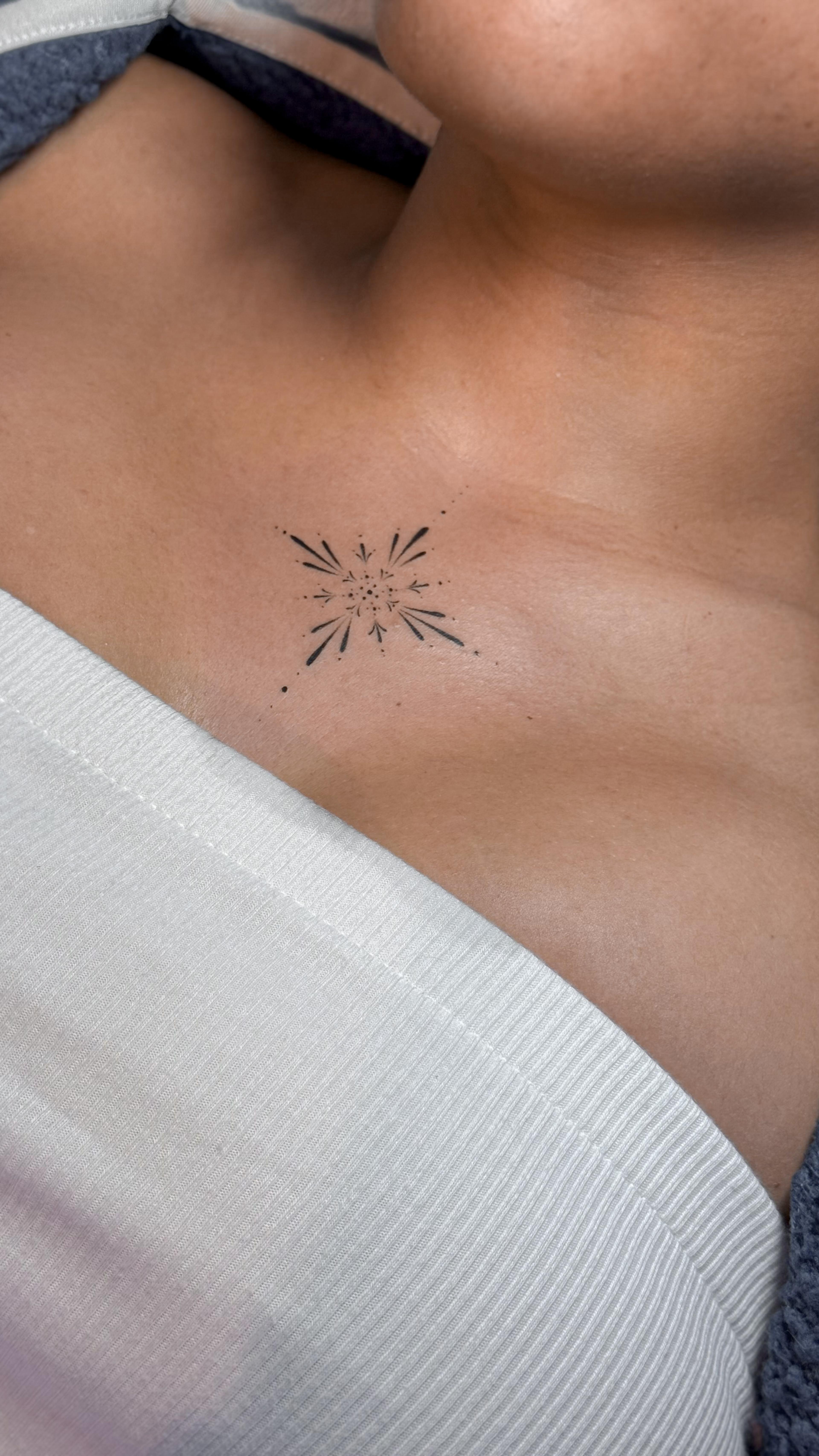 Small ornamental starburst tattoo on the middle of the chest
