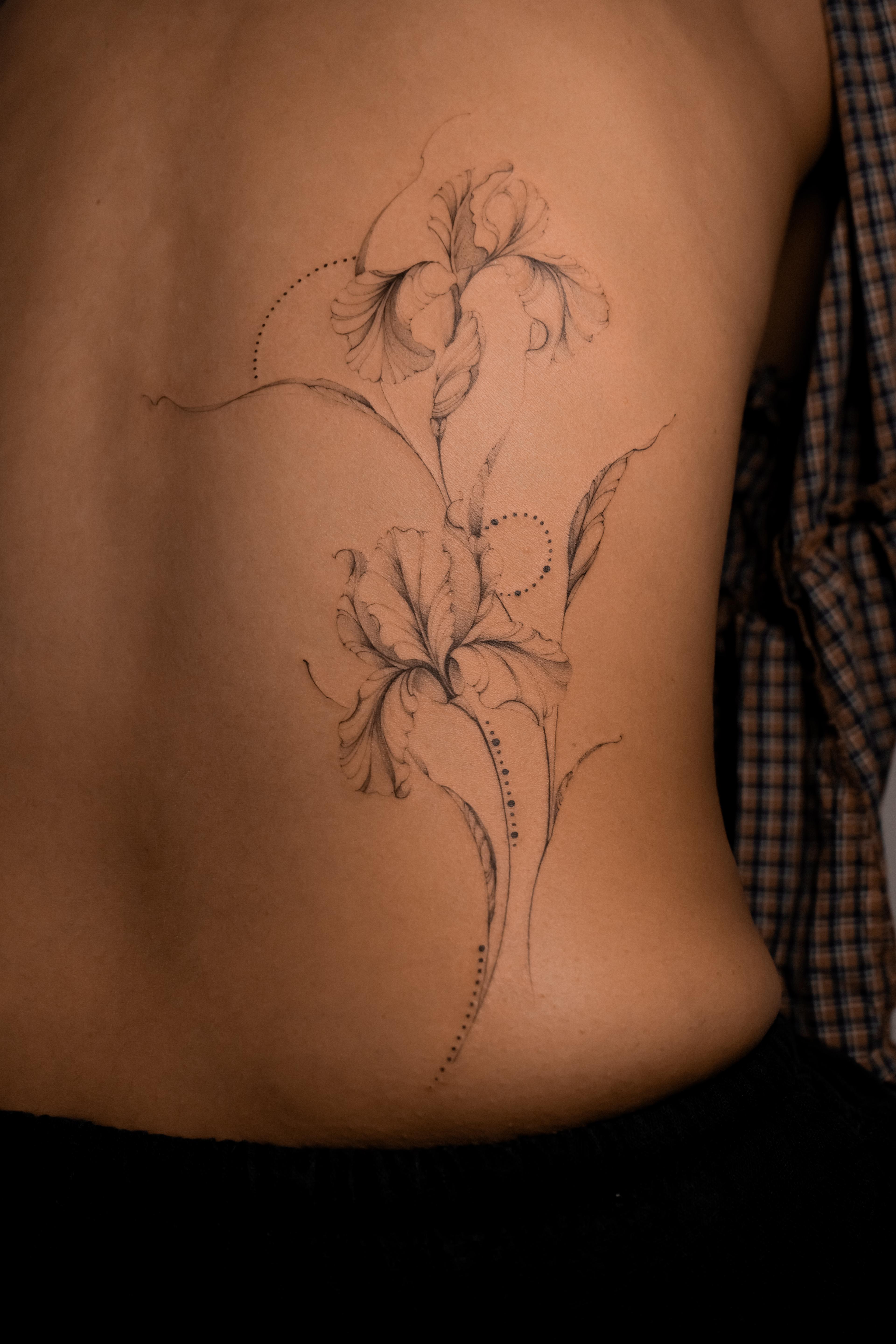 Fine-line iris flowers and delicate dotwork flowing along the lower back