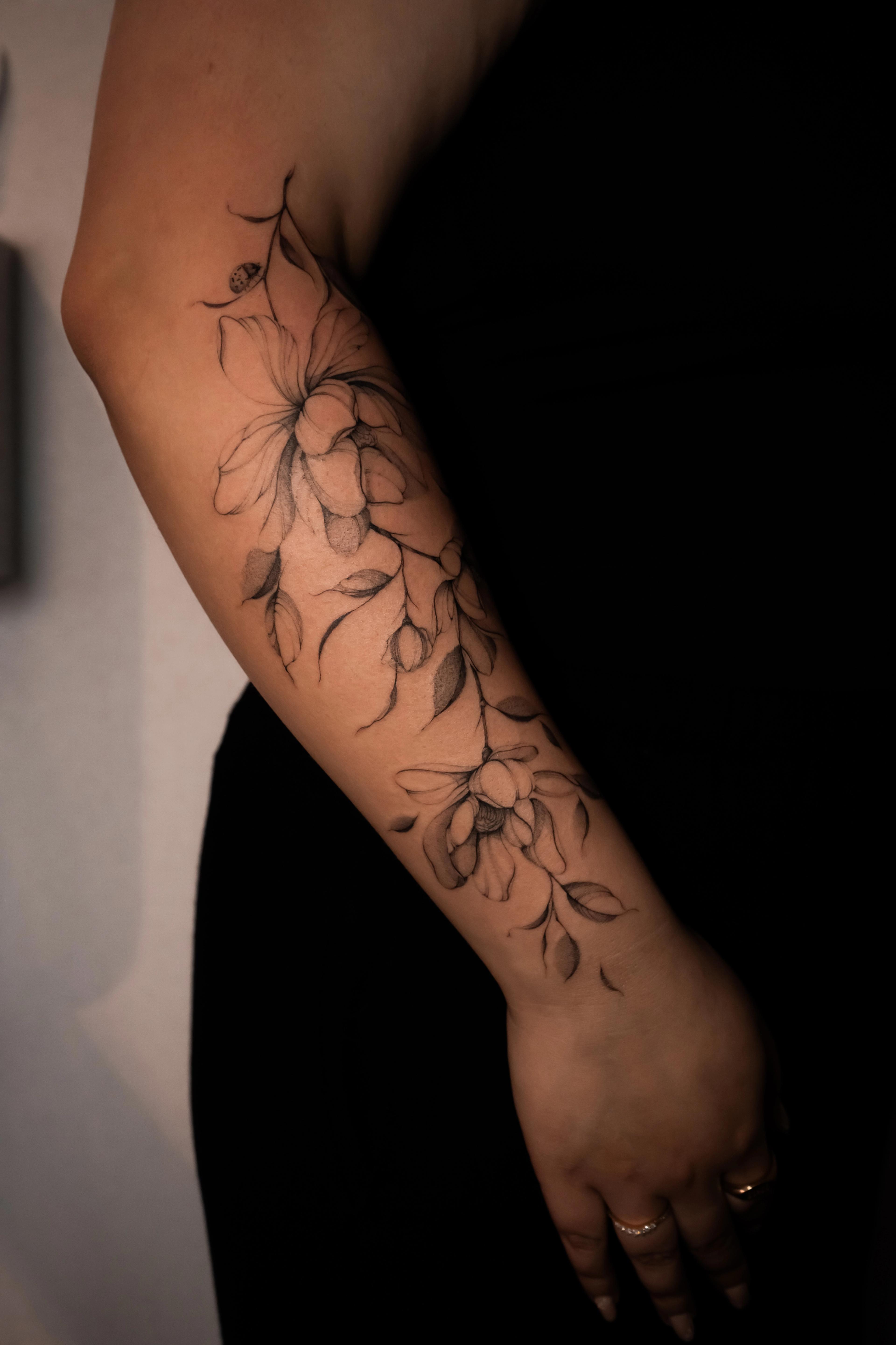 Fine-line magnolia and falling leaves with a small ladybug on the forearm