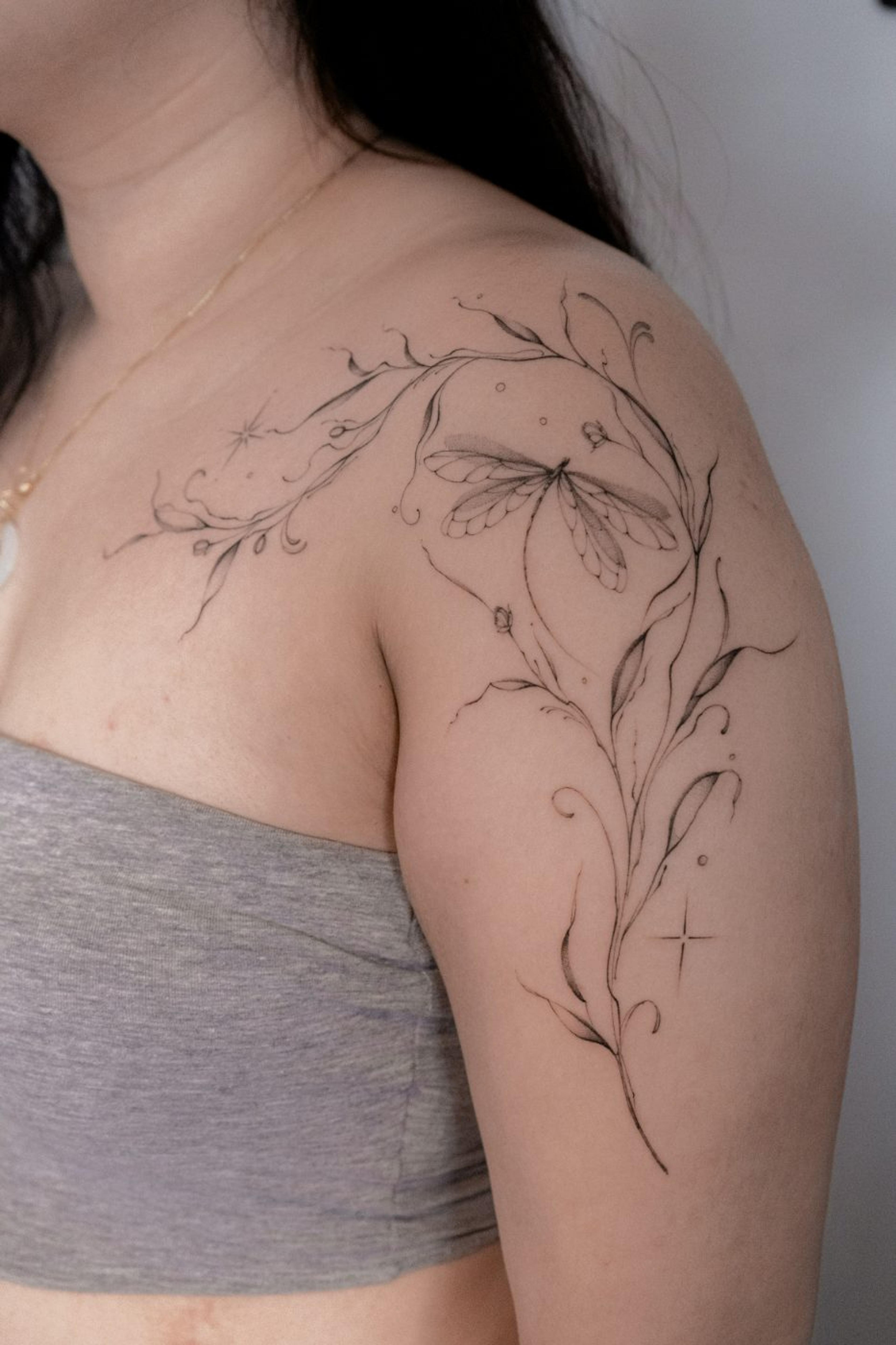 Fine-line dragonfly with trailing vines across shoulder and clavicle