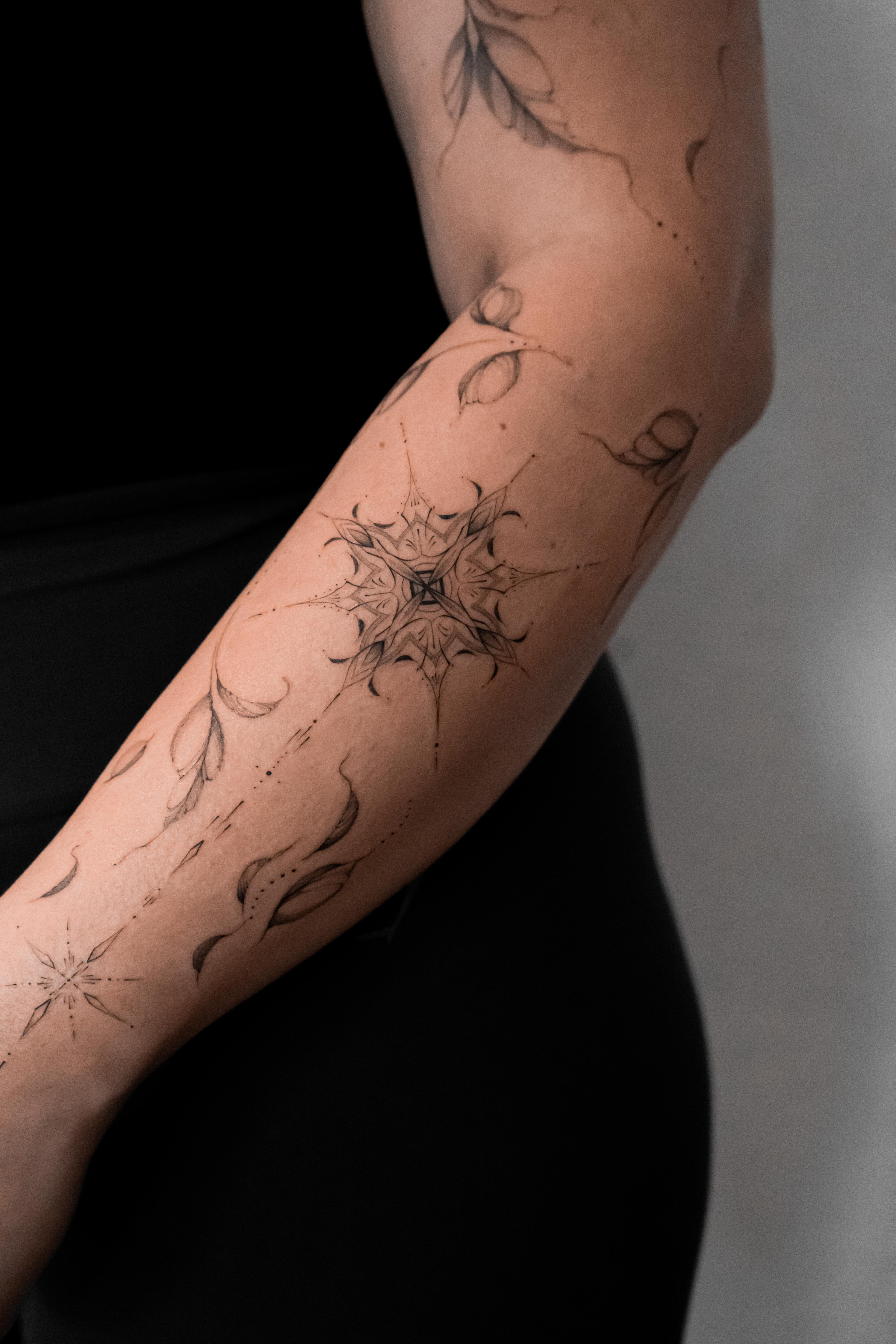 Fine-line geometric, ethereal floral motifs along the forearm