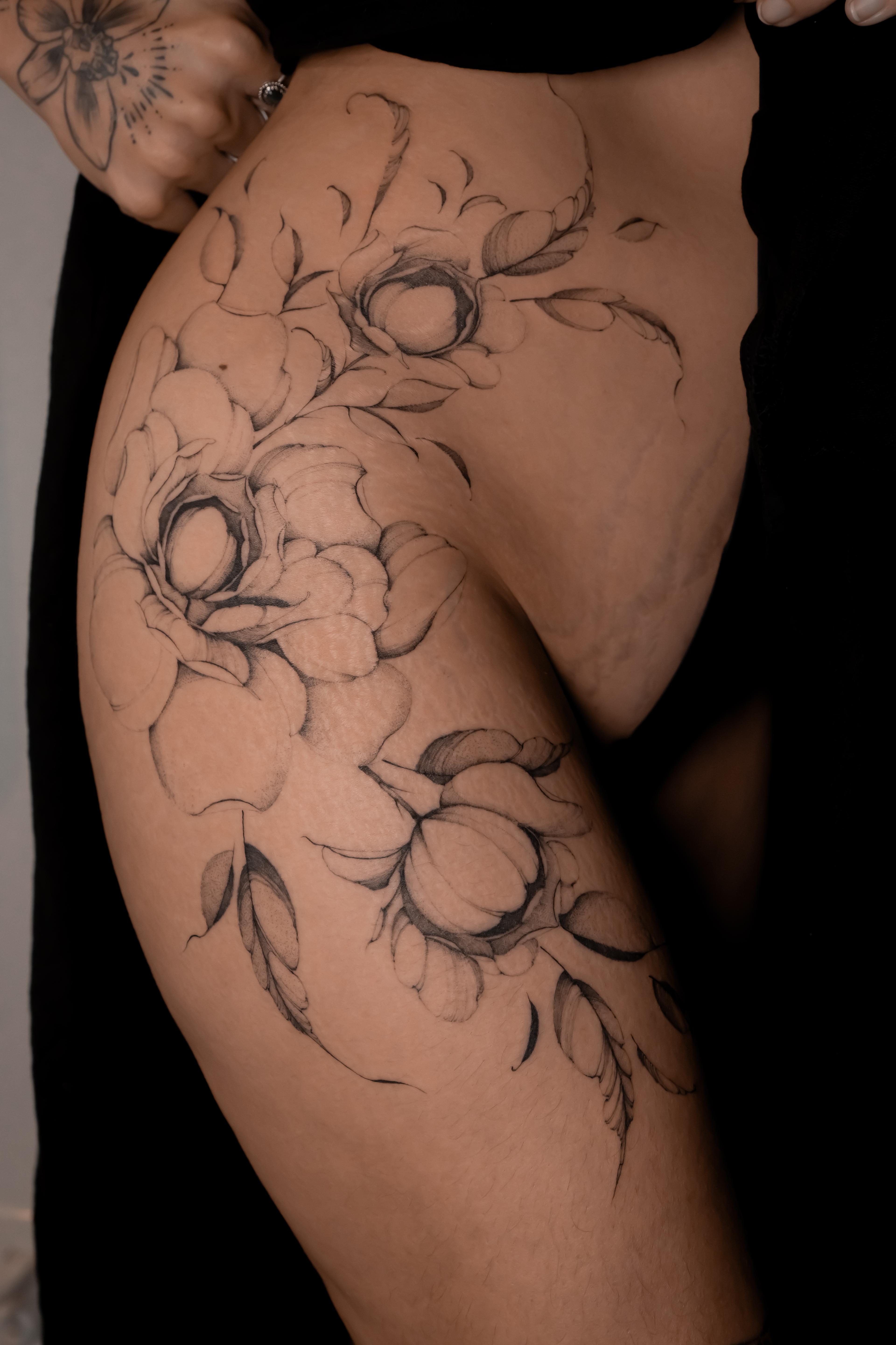 Large fine-line peonies flowing across the hip and upper thigh