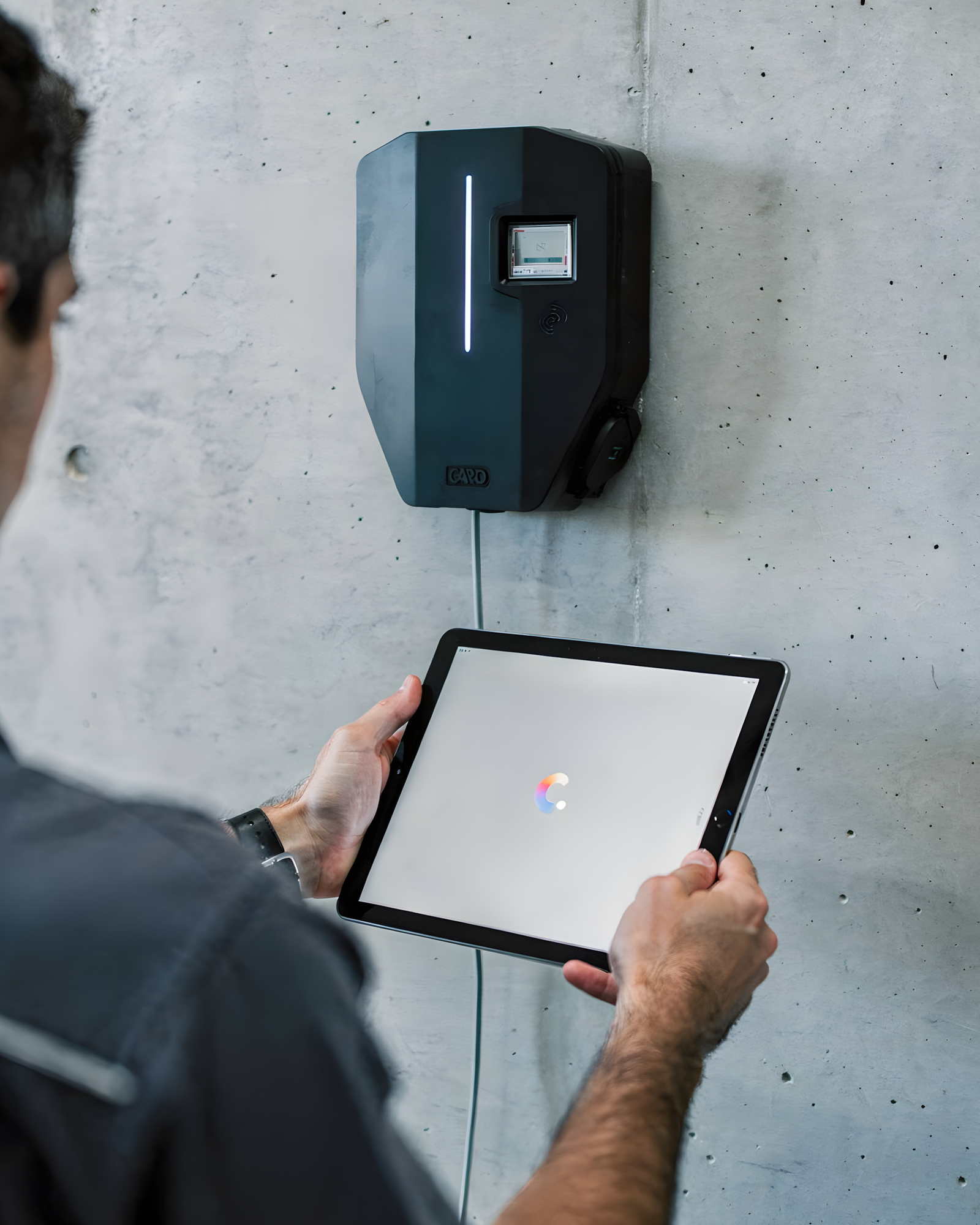 Techniker mit Tablet vor einer an der Betonwand montierten Ladestation