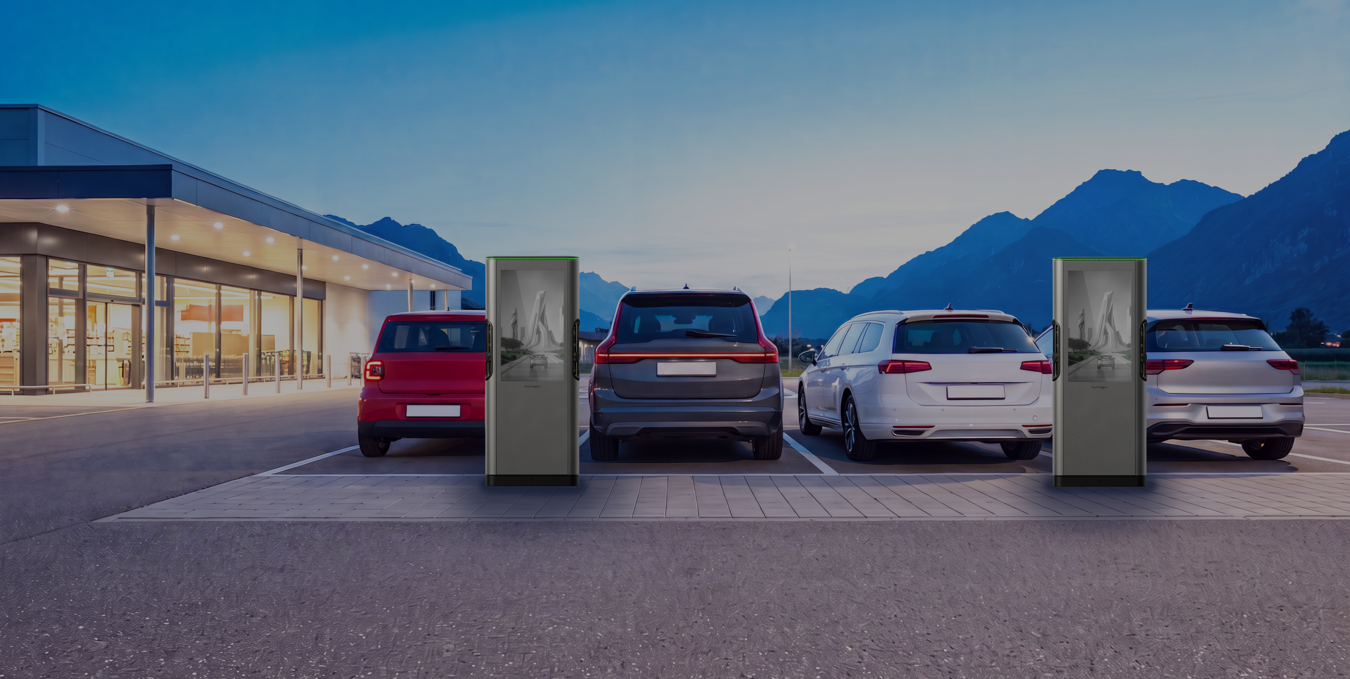 Kundenparkplatz vor einem beleuchteten Ladengeschäft, drei Fahrzeuge an Ladesäulen in der Dämmerung