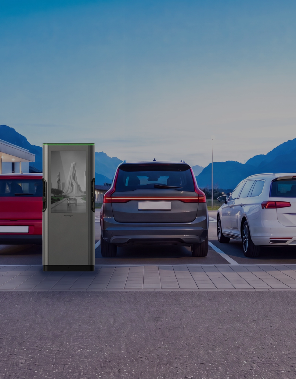 Kundenparkplatz vor einem beleuchteten Ladengeschäft, drei Fahrzeuge an Ladesäulen in der Dämmerung