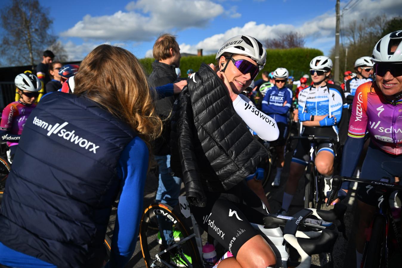 The former two-time world champion Anna van der Breggen hands the current world champion a jacket, as Lotte Kopecky tried to stay warm during the interruption 