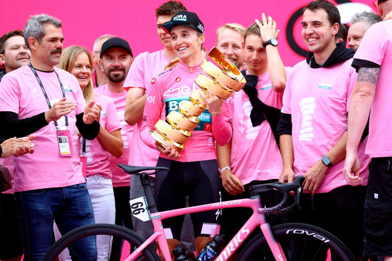 Denk (left) watches on as Jai Hindley lifts the 2022 Giro d'Italia trophy - his team's first Grand Tour victory