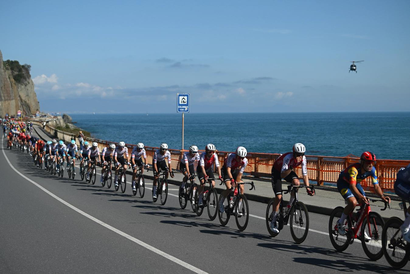 The peloton strings out on the coast road