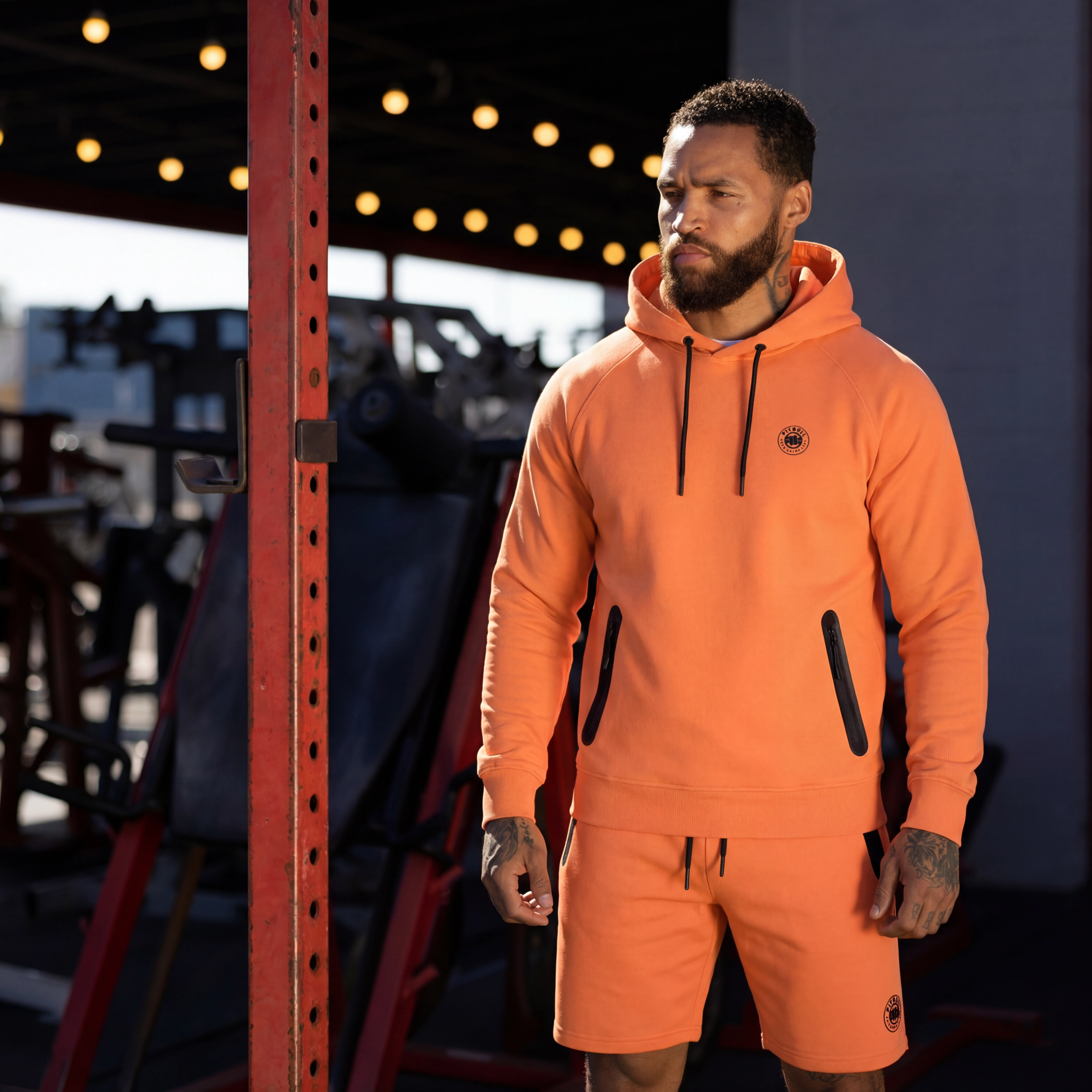 Man in a bright orange hoodie and shorts in a gym