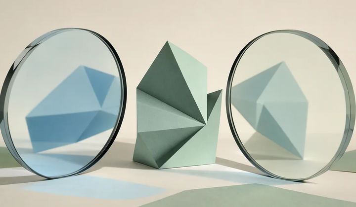 A mint angular sculpture viewed through two clear lenses from opposing sides, revealing different pale blue shadows on an ivory background