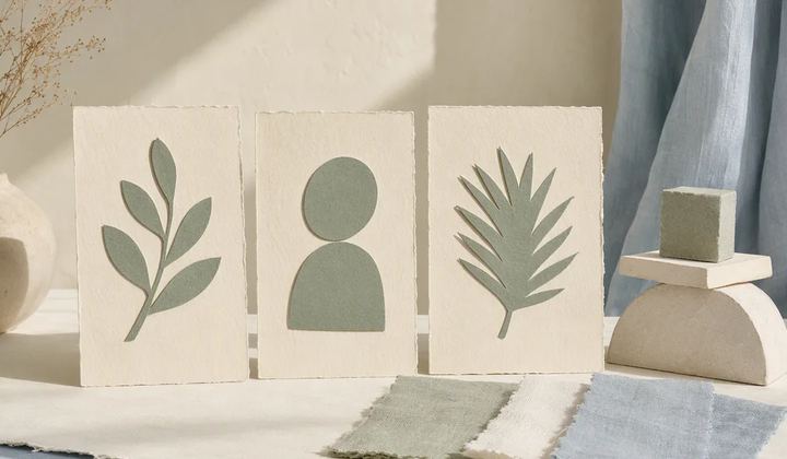 Three cream cards with sage plant and person motifs beside a small display stand and fabric swatches.