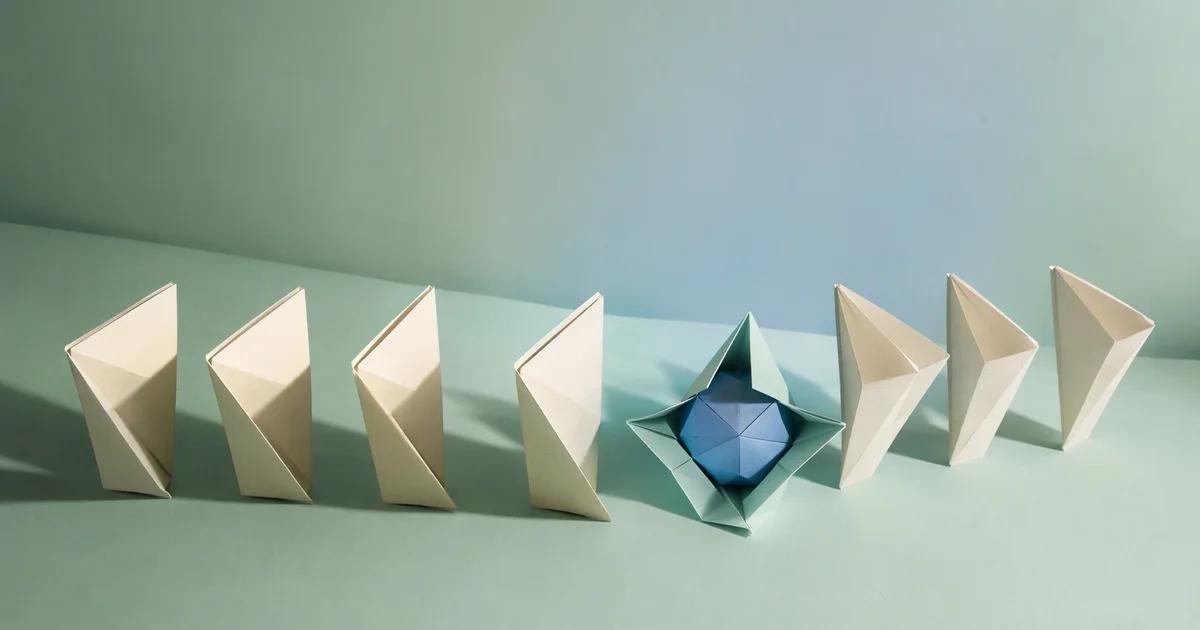 A row of ivory folded paper forms surrounds an open mint fold containing a blue geometric shape.