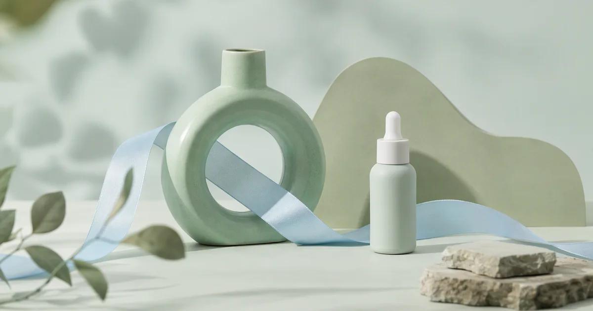 An unlabeled bottle beside a blue ribbon passing through a green ceramic ring.