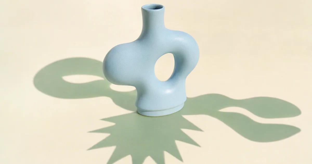One central pale blue ceramic form casts three distinctly shaped mint shadows across a warm ivory surface.