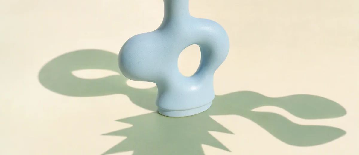 One central pale blue ceramic form casts three distinctly shaped mint shadows across a warm ivory surface.