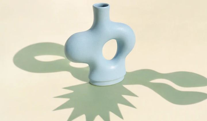 One central pale blue ceramic form casts three distinctly shaped mint shadows across a warm ivory surface.