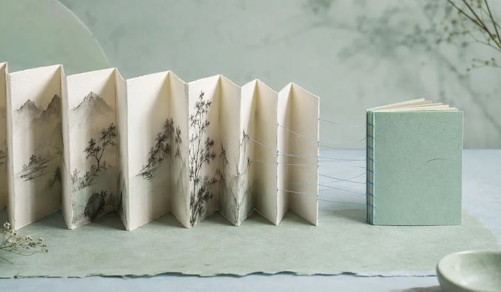 A large ivory accordion book narrowing into a compact mint booklet while several pale blue threads remain visibly connected between them