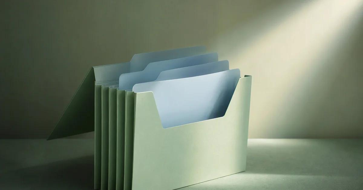 A mint accordion folder holds several pale blue dividers, with its front section lit by a focused beam.