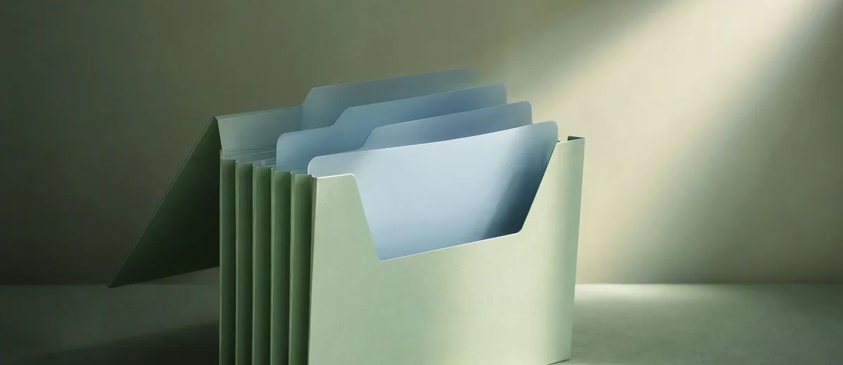 A mint accordion folder holds several pale blue dividers, with its front section lit by a focused beam.
