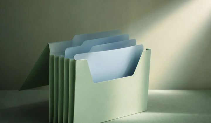A mint accordion folder holds several pale blue dividers, with its front section lit by a focused beam.
