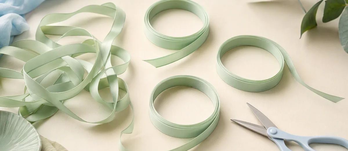 Several tangled mint ribbons being separated into three clean loops on an ivory table, with pale blue scissors resting nearby