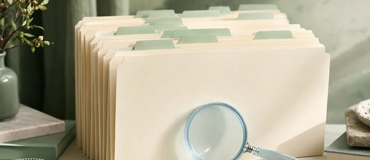 A carefully arranged archive of ivory folders with mint tabs and one pale blue glass magnifier, photographed in soft side light