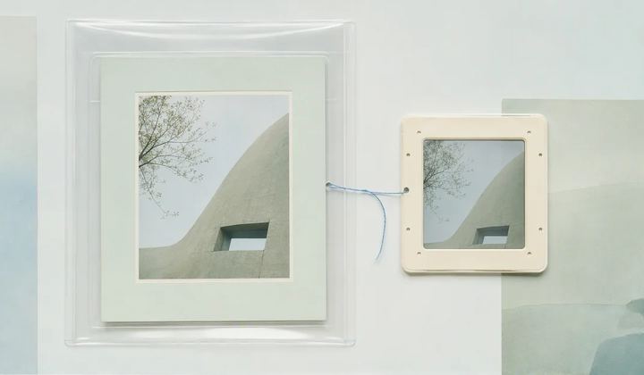 A photographic print in a transparent sleeve linked by blue thread to a smaller framed copy.