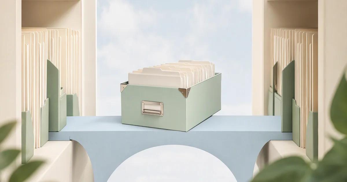 A mint archive box filled with ivory folders rests on a pale blue bridge between two ivory shelves.