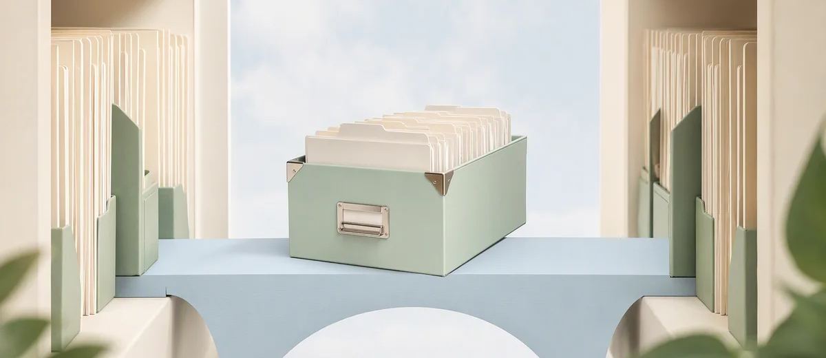 A mint archive box filled with ivory folders rests on a pale blue bridge between two ivory shelves.