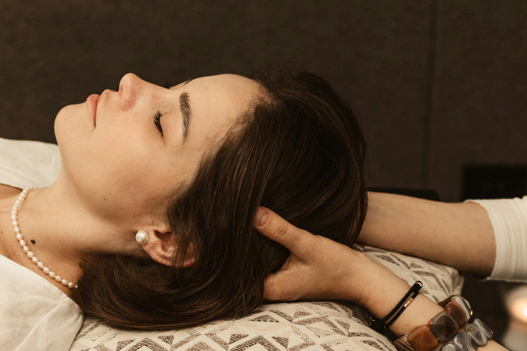 Woman lying on a patterned pillow with her eyes closed while a therapist massages the back of her head