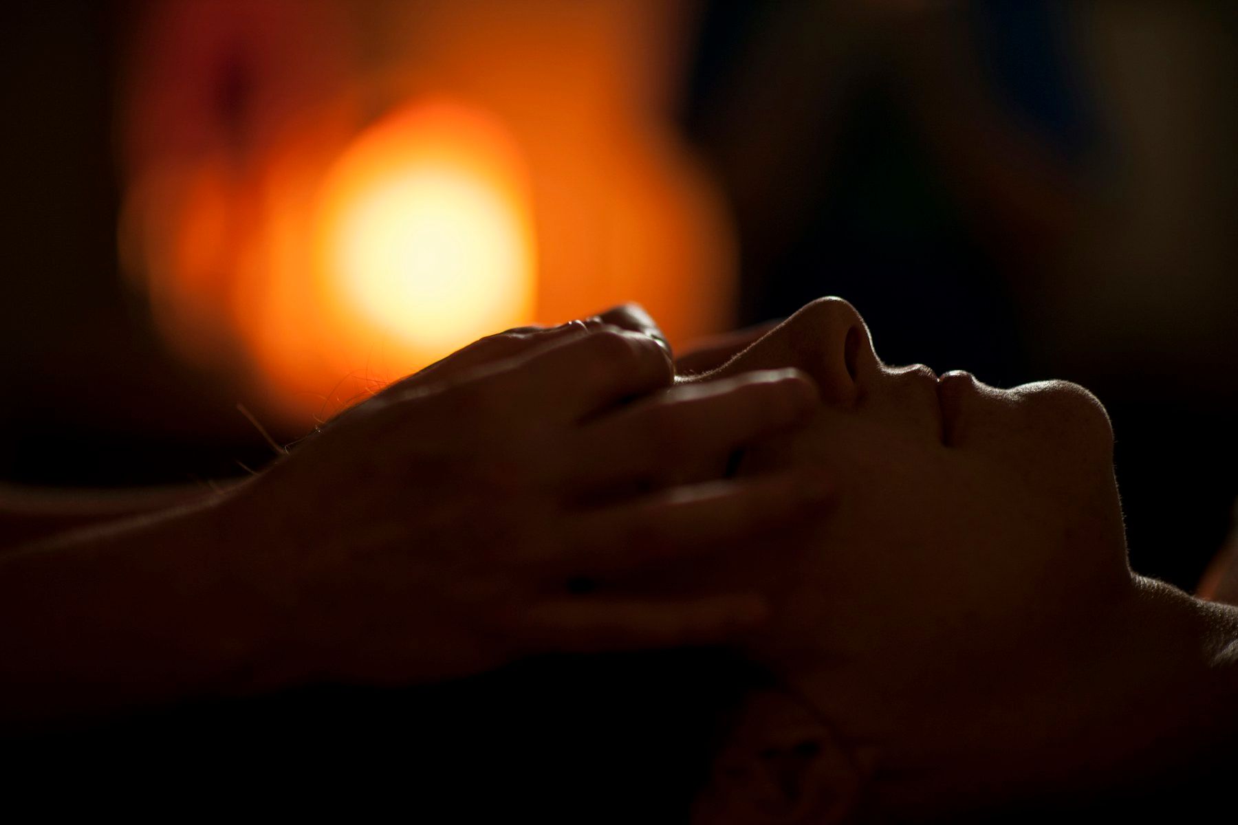 Therapist's hands massaging a relaxed client's temples in a dimly lit treatment room