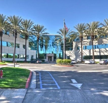 Exterior view of the office building at 25909 Pala Street in Mission Viejo, California, with a landscaped entrance, palm trees, and parking lot.