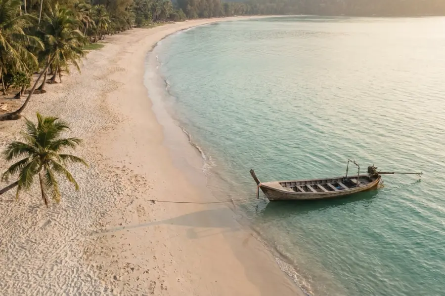 A long quiet stretch of white sand on Phuket's west coast at golden hour with limestone headlands and no people in sight