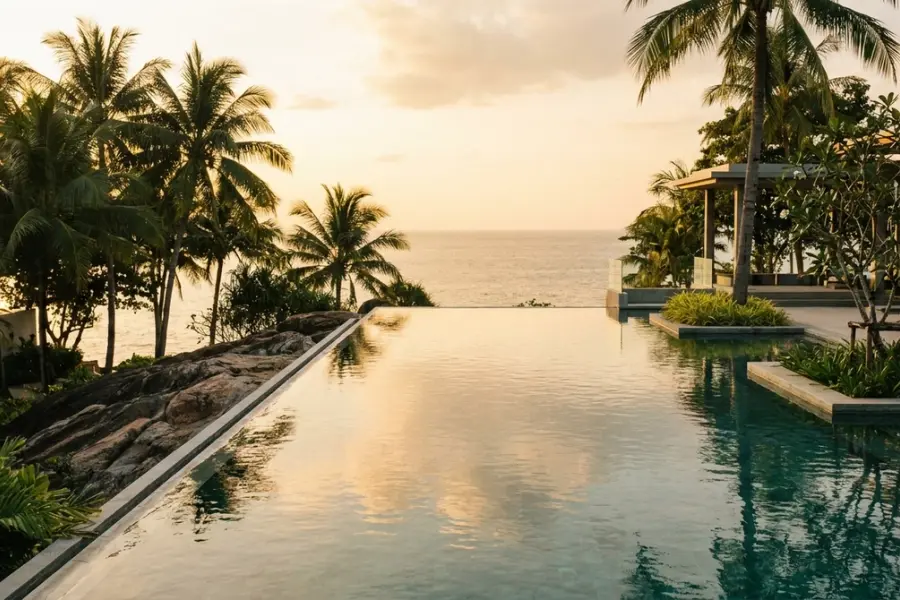 A long wooden villa table set with mineral water and notebooks overlooking the Andaman Sea at golden hour