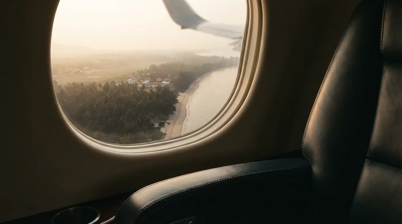 A leather-seat foreground and palm-coastline view through a private jet window on descent into Hua Hin