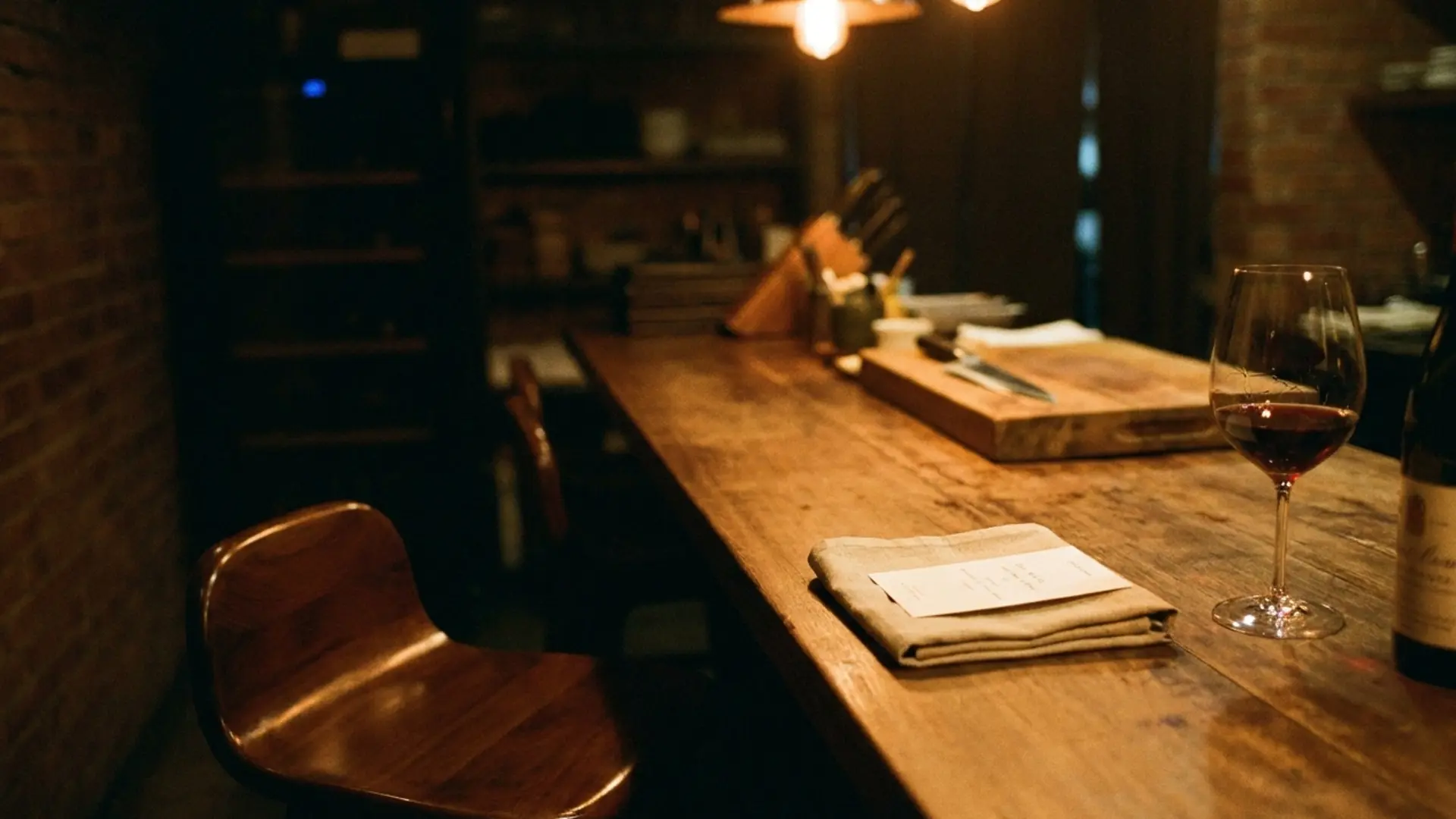 An empty corner banquette in a candlelit Bangkok private dining room, single reserved card on starched white linen