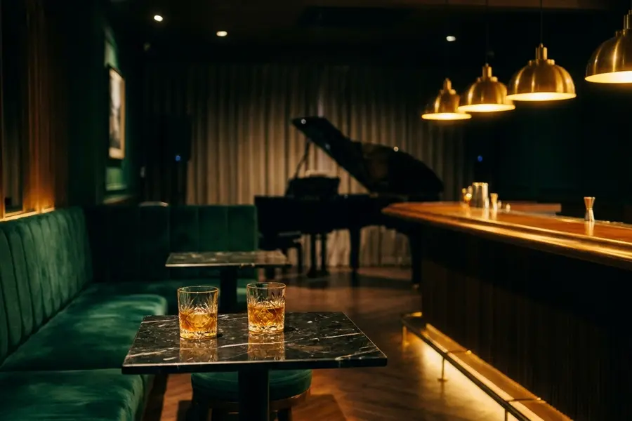 A dimly lit Bangkok cocktail bar after midnight with low brass pendants over an empty marble bar and a row of crystal glasses