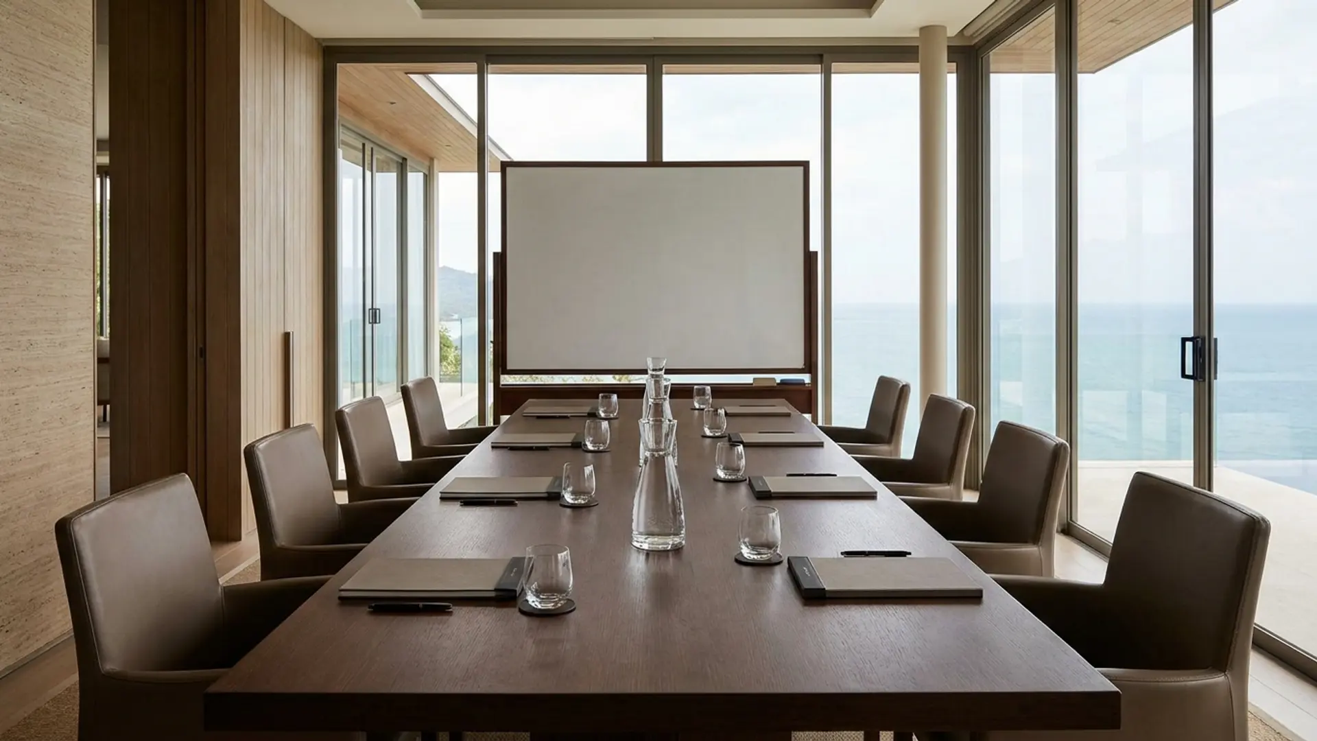 A private villa boardroom — long walnut table, eight Aeron chairs, a wall of glass overlooking a tropical garden