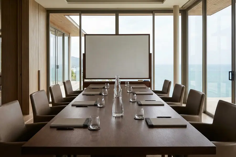 A private villa boardroom — long walnut table, eight Aeron chairs, a wall of glass overlooking a tropical garden